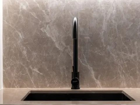 A black kitchen faucet over an undermount sink against a marble wall