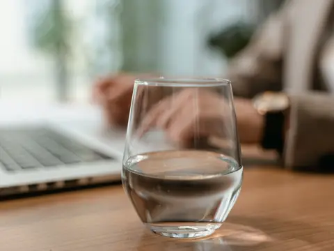 A glass of water on an office desk beside a laptop