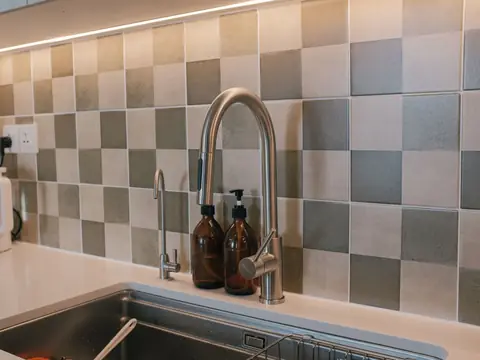A kitchen sink with a tall faucet and a small second faucet under a checkered tile backsplash