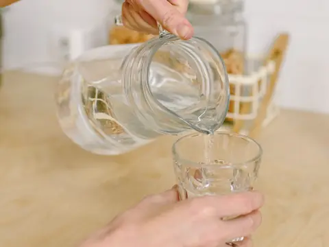 Water poured from a glass jug into a glass at a wooden table