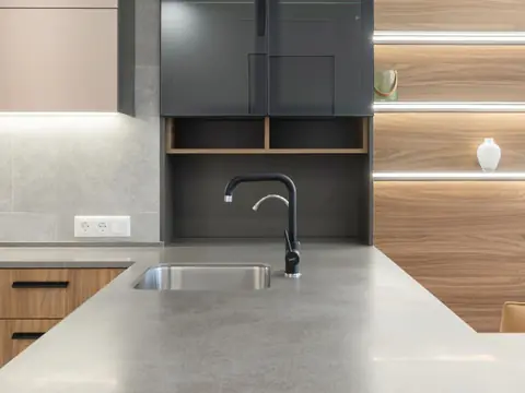A kitchen with a black faucet over a steel sink and warm cabinet lights