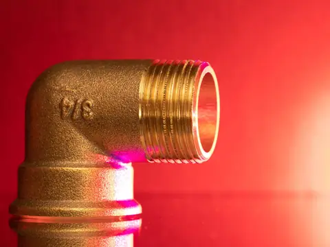 A threaded brass elbow fitting against a red background