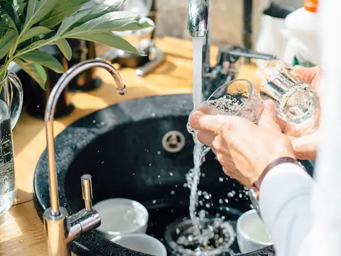A glass rinsed at a black kitchen sink, a slim drinking water faucet standing beside the main tap