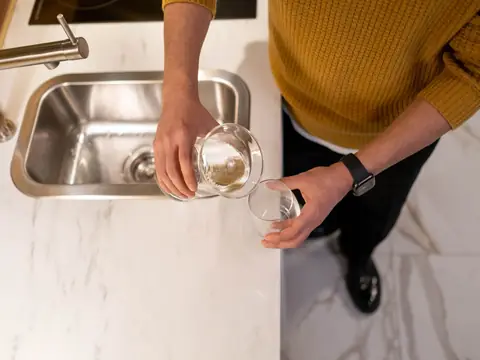 Water poured into a glass over a steel kitchen sink
