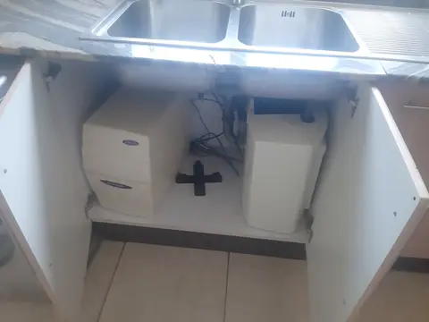 A water filter system and its tank set inside an open kitchen sink cabinet