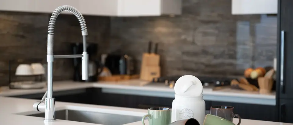 A bright kitchen counter with a sink, a faucet and mugs