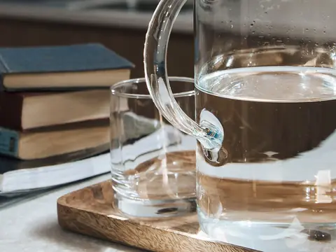 A glass jug of water and a glass on a wooden tray in sunlight