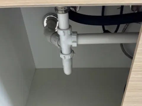Inside an empty kitchen sink cabinet, with the drain pipes under the sink