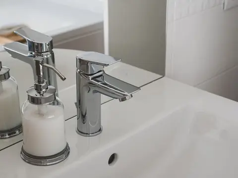 Chrome faucets and a soap dispenser at a white basin