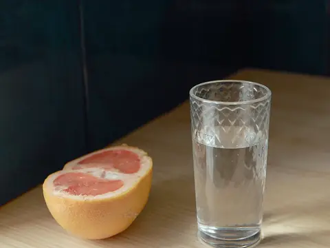 A glass of water beside half a grapefruit on a light table
