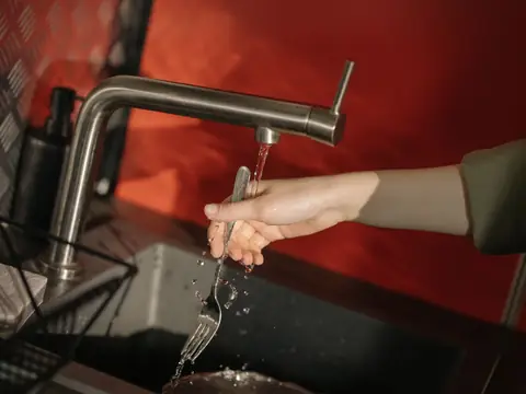 Water running from a steel tap over a fork into a dark sink