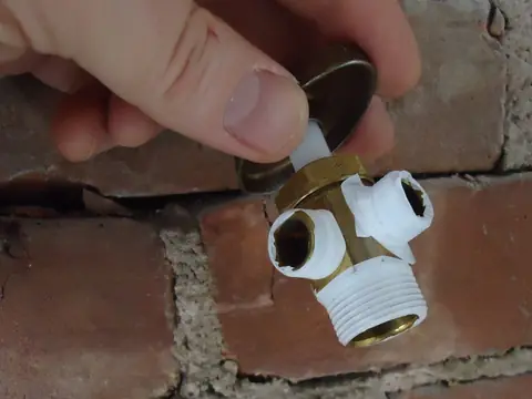 A hand fitting a new brass valve with white thread tape onto a water pipe