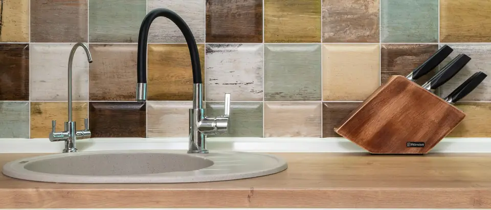 A slim chrome drinking water faucet beside a black kitchen faucet over a sink