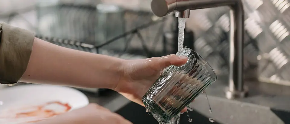A glass rinsed under a running tap at a kitchen sink