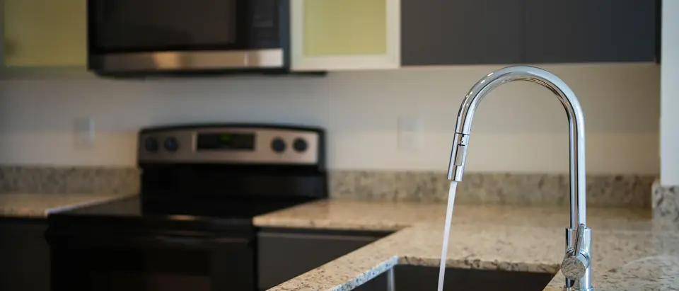 Water running from a kitchen faucet into a sink set in a granite counter