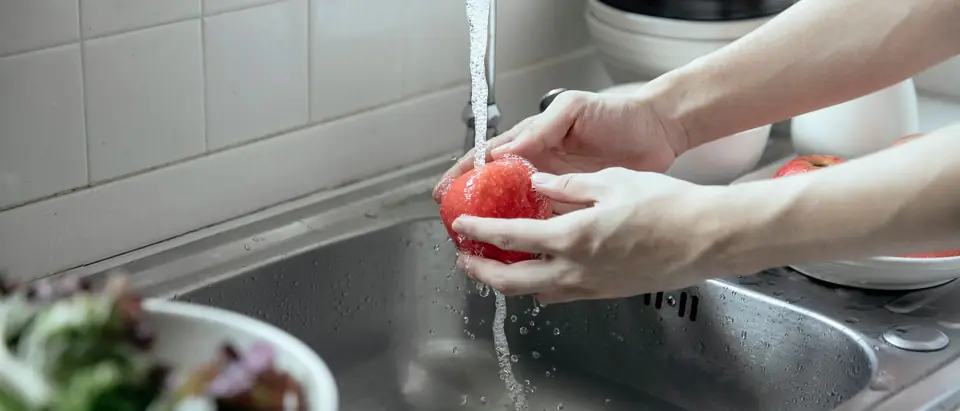 Water running from a kitchen tap over an apple into a steel sink