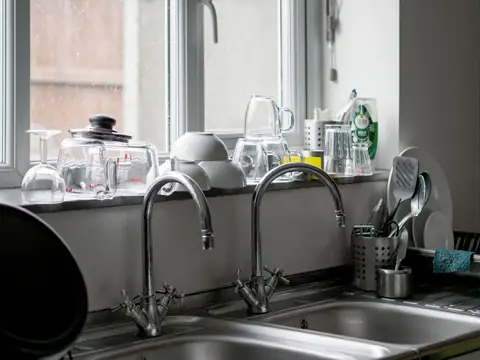 Two kitchen faucets over a steel double sink below a window
