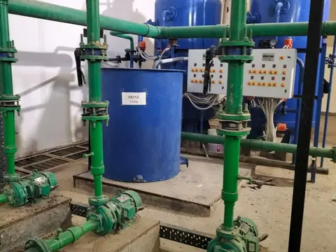 Blue water softening tanks and a brine tank joined by green pipes and pumps in a plant room
