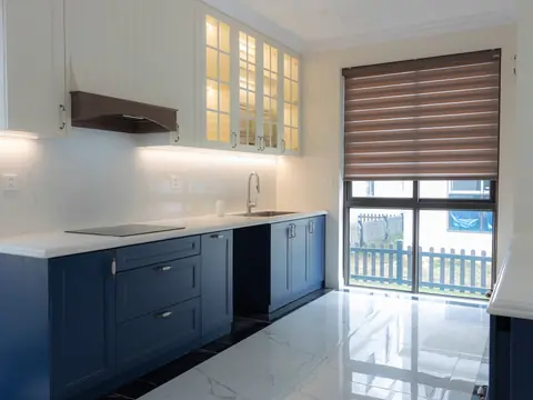 A bright kitchen with blue lower cabinets and a window to a garden