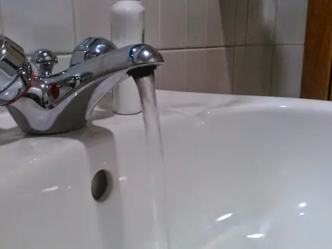 Water running from a chrome bathroom tap into a white basin